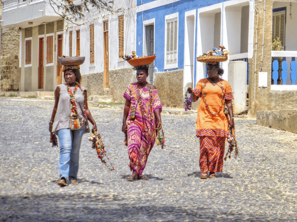  Três locais cabo-verdianas, atarefadas com tarefas/ trabalho, a percorrer uma estrada de calçada